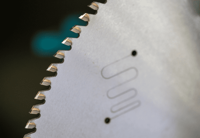 Macro shot of a non-ferrous circular saw blade, focusing on the tooth profile and laser-etched expansion slots designed to reduce vibration during aluminium cutting.